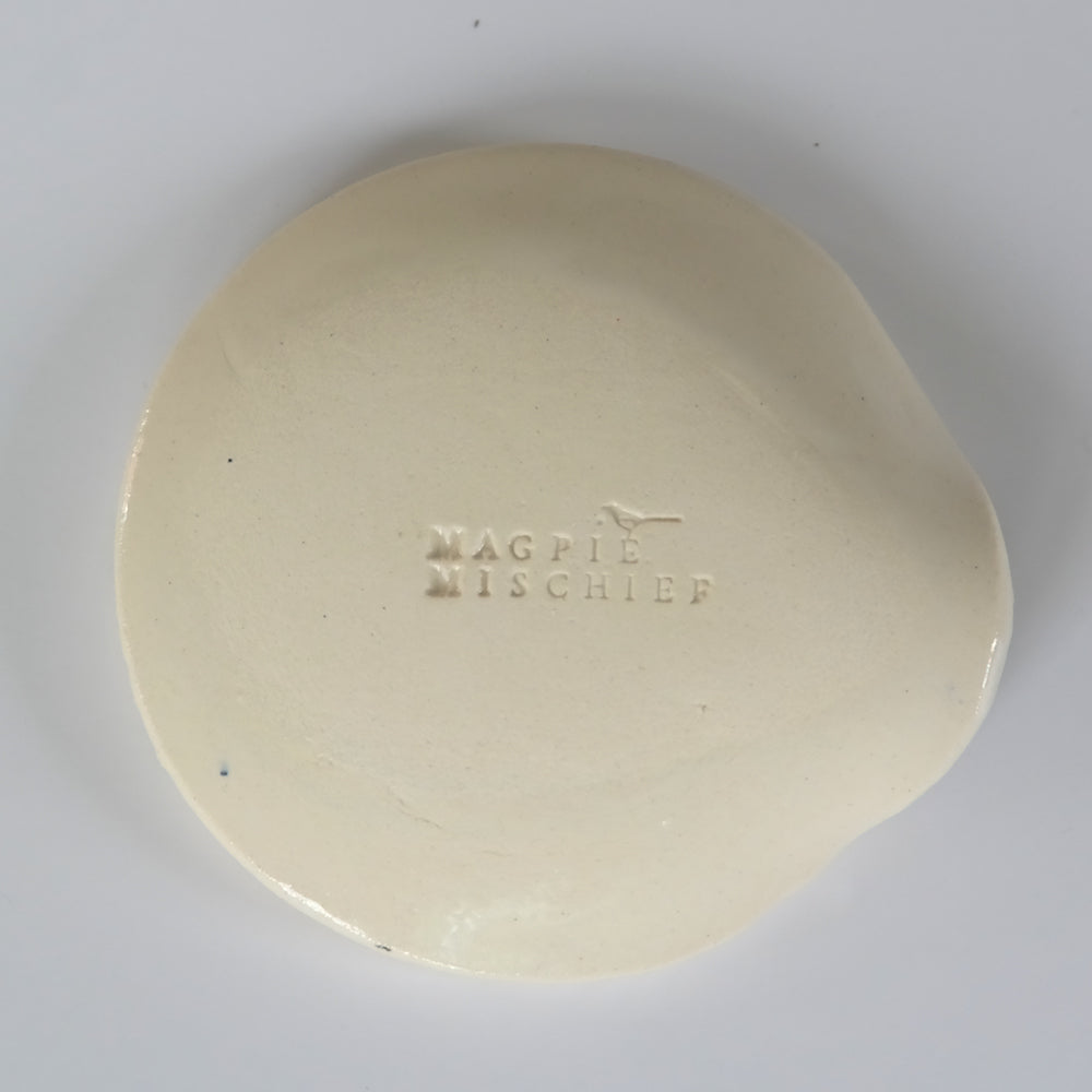 Back view of round ceramic spoon plate with the inscription "magpie mischief"
