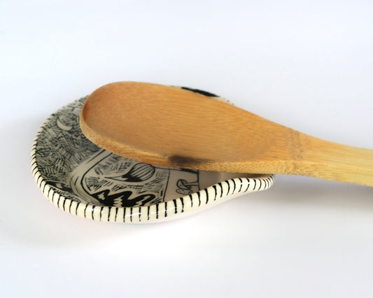 Ceramic spoon plate with decorative black and white fox design on a white background, and a wooden spoon on it