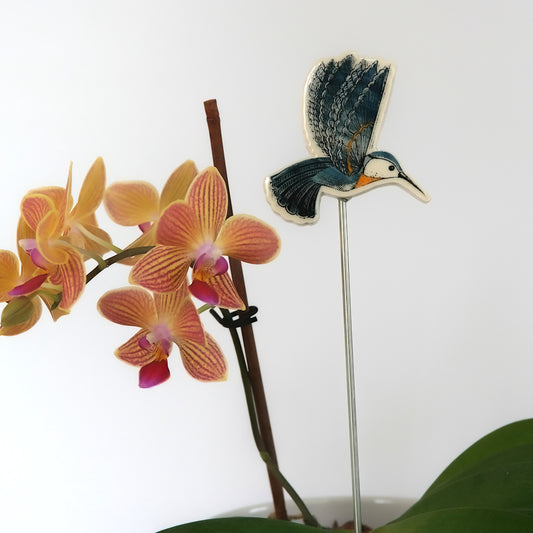 Decorative garden stake with a blue hummingbird design and orange orchids on a white background