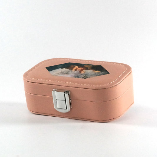 Miniature pink jewelry box with a button closure and a hexagonal paint of a woman reading a book to two girls, pictured from the side.