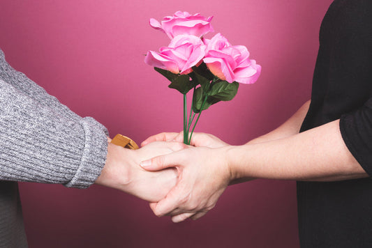 man and women grabbing hands and plastic pink roses in the middle of the photo, on a pink background.