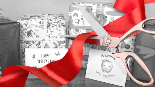 Scissors cutting a ribbon in front of a grey image with wrapped gifts..