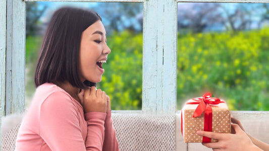 Woman smiling while getting a gift in front of a window with a flowery background. 