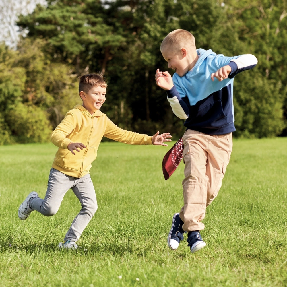 Two children running outdoors while using a red bandana during an active group game.