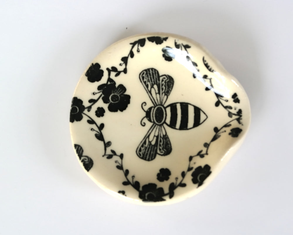 Round ceramic spoon plate with a bee design on a white surface