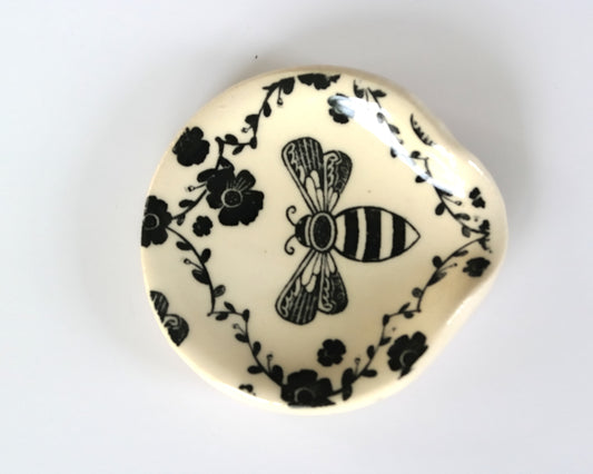 Round ceramic spoon plate with a bee design on a white surface
