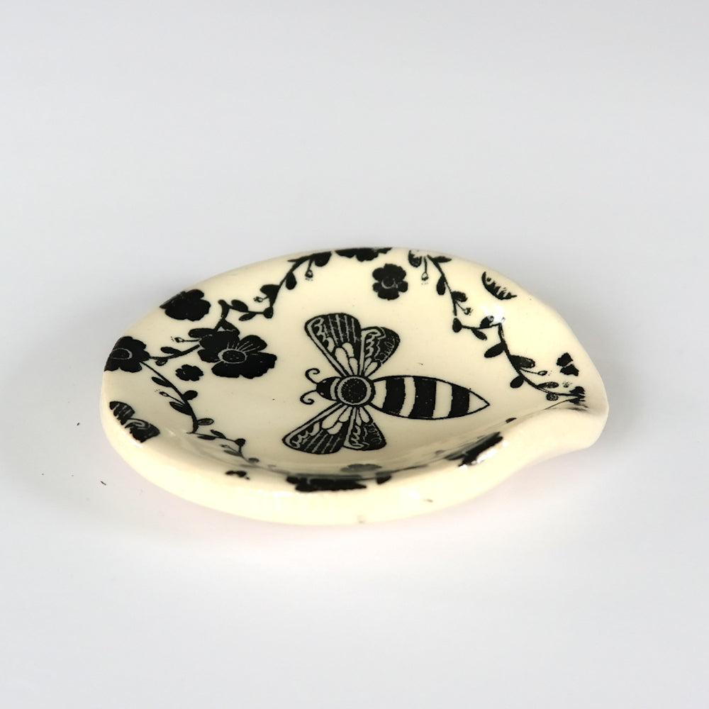 Side view of round ceramic spoon plate with a bee design on a white surface