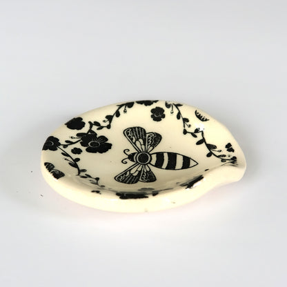 Side view of round ceramic spoon plate with a bee design on a white surface