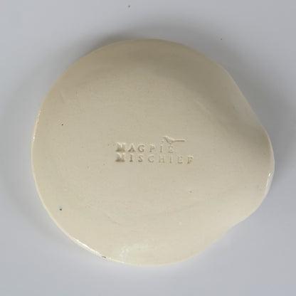 Back view of round ceramic spoon plate with the inscription "magpie mischief"