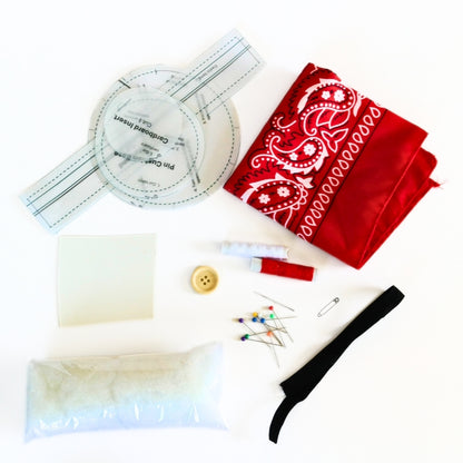 Flower pin cushion wristband kit materials with bandana fabric, pattern pieces, stuffing, elastic, button, pins, needle, and thread.