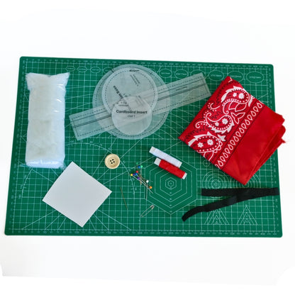 Lifestyle image of flower pin cushion wristband kit materials with bandana fabric, pattern pieces, stuffing, elastic, button, pins, needle, and thread.