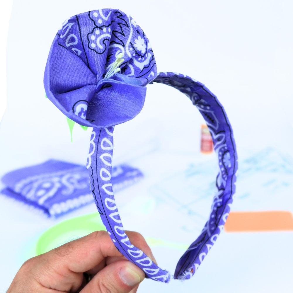 Purple bandana headband with a flower detail attached in front of the DIY materials used to make it.  
