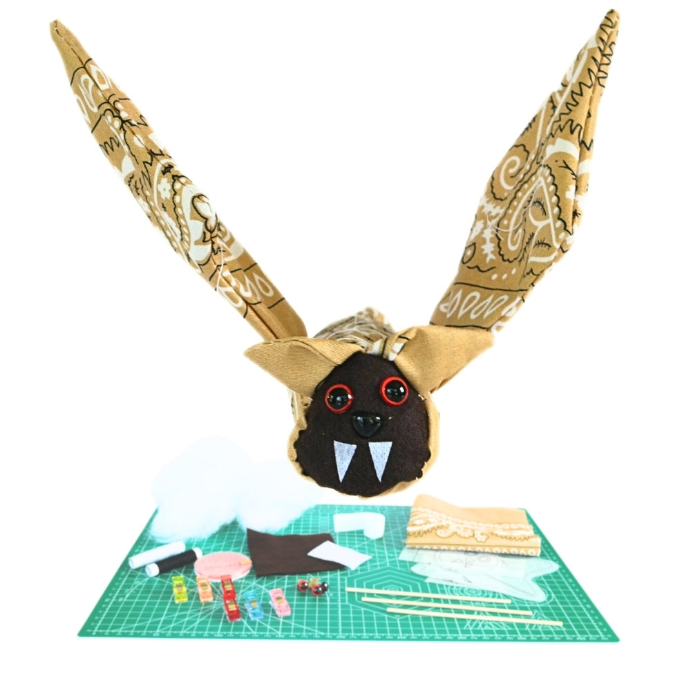 Bandana Flying Bat DIY kit showing the finished tan paisley bat above the fabric, stuffing, patterns, rods, sewing clips, and other included craft supplies.