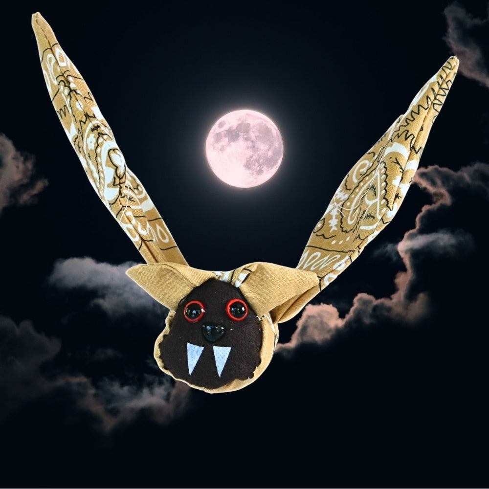 Finished tan bandana bat with raised wings displayed against a dark Halloween night sky with clouds and a full moon.