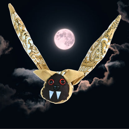Finished tan bandana bat with raised wings displayed against a dark Halloween night sky with clouds and a full moon.