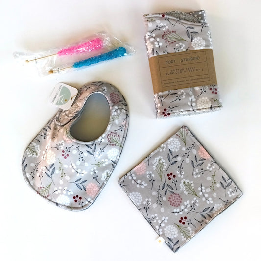 Baby gift set with a bib, burp clothes, crinkle toy, and rock candies on a white background