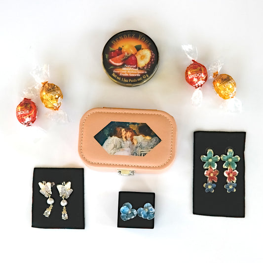 Collection of earrings, a a keepsake box, chocolate truffles and a tin of candy on a white surface with decorative candies.