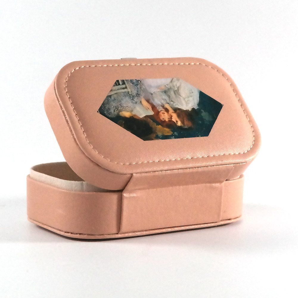 Miniature pink jewelry box with a button closure and a hexagonal paint of a woman reading a book to two girls, pictured from the back. 