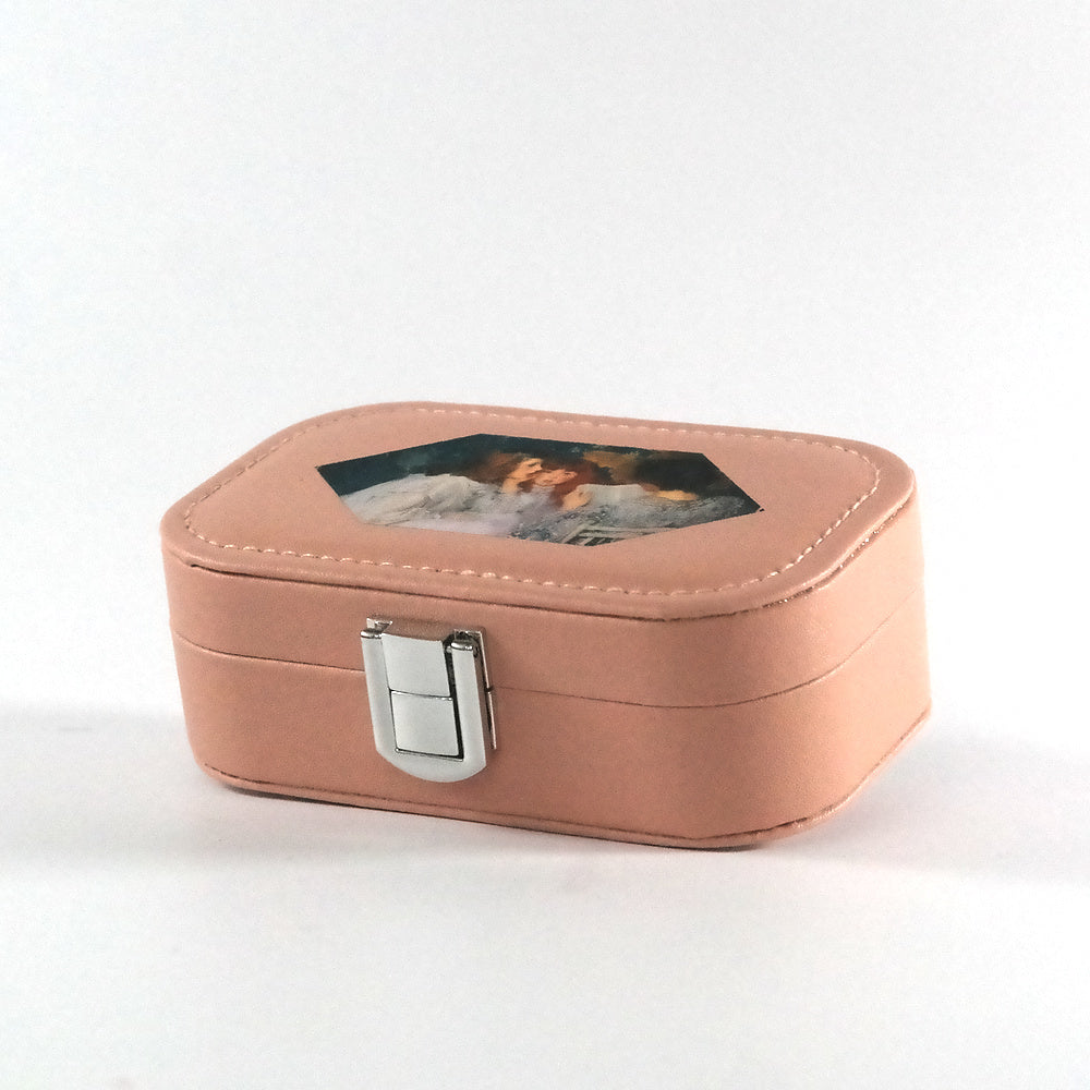 Miniature pink jewelry box with a button closure and a hexagonal paint of a woman reading a book to two girls, pictured from the side. 