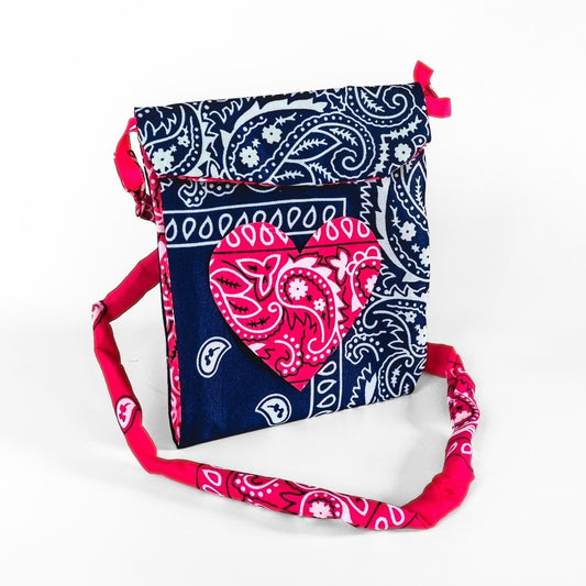 A fabric crossbody bag featuring a navy blue and white paisley bandana pattern, with a bright pink heart-shaped bandana patch on the front and a matching pink and white paisley shoulder strap.