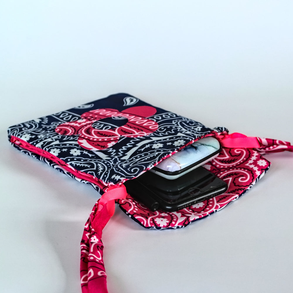 A bandana bag with a navy, pink, and white paisley pattern, shown open with a smartphone tucked inside. The sleeve features a matching pink and white paisley ribbon strap on a white background.