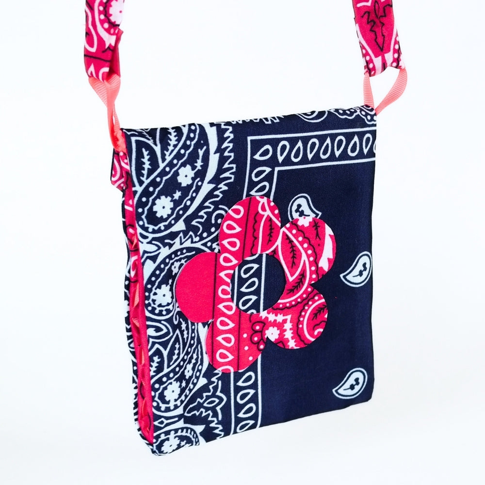 A bandana print shoulder bag featuring a navy blue and pink paisley pattern with a large pink bow graphic on the front, set against a plain white background.