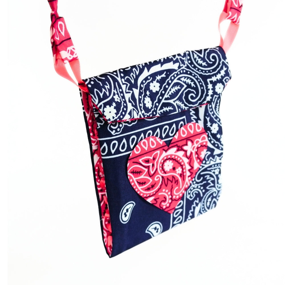 A small crossbody bag made from navy blue and red paisley bandana fabric, featuring a red heart-shaped patch on the front pocket and matching patterned straps, shown against a plain white background.