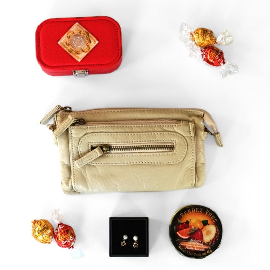 Beige handbag with a red jewelry box, earrings, and a small container on a white background