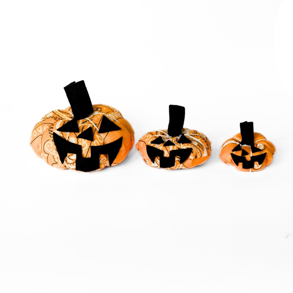Three orange bandana pumpkins with optional black felt jack-o’-lantern faces on a white background