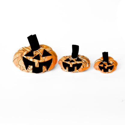 Three orange bandana pumpkins with optional black felt jack-o’-lantern faces on a white background
