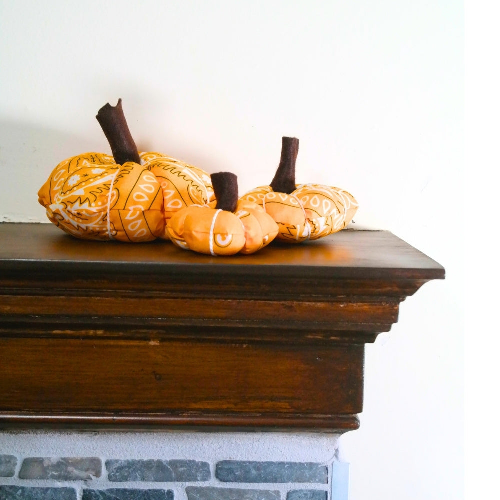 Three handmade bandana pumpkins displayed together on a wooden mantel for fall decorating